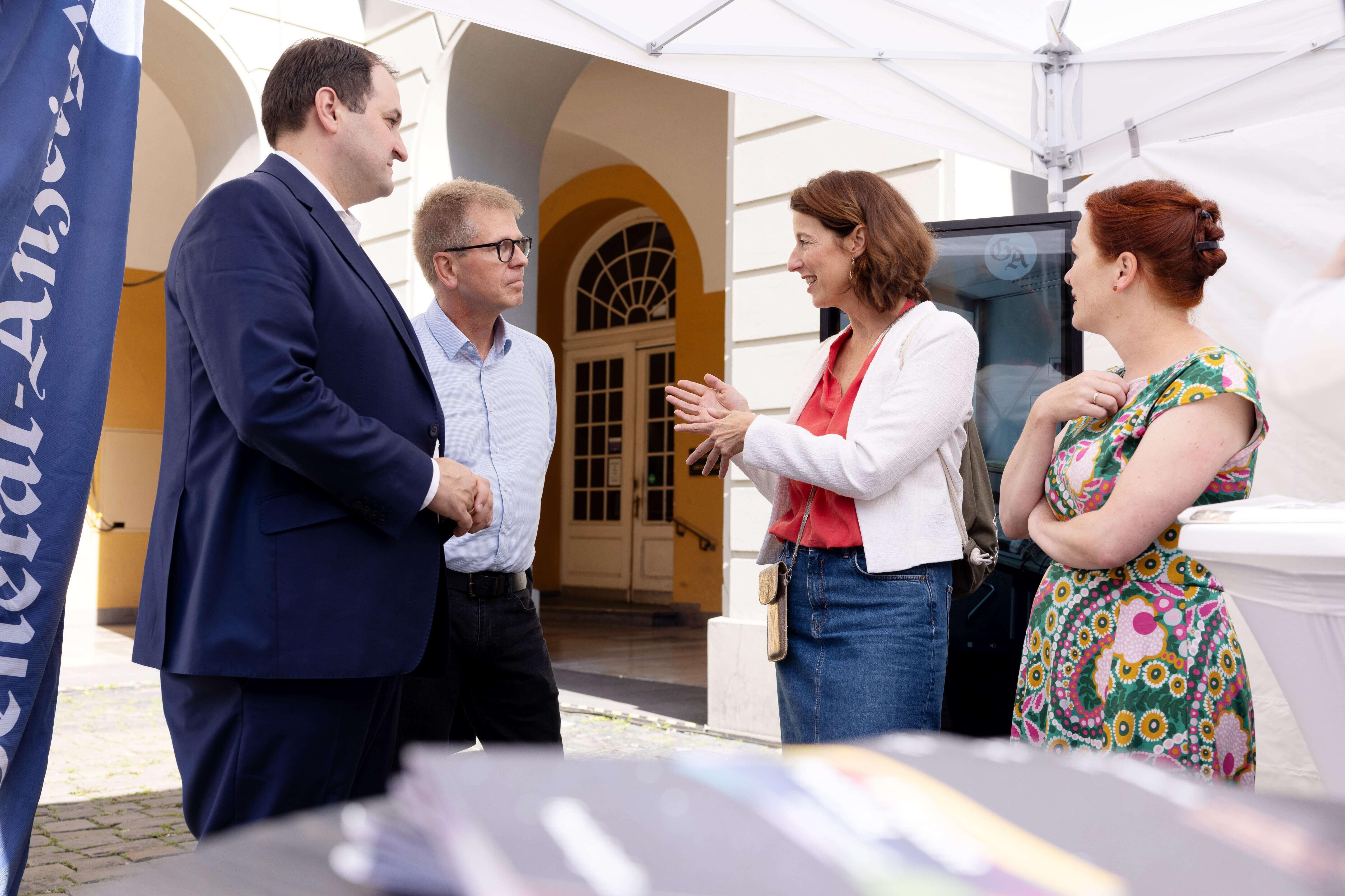 Von links nach rechts stehen Nathanael Liminski, Helge Matthiesen, Ellen Heinrichs und Katja Dörner zusammen unter einem Pavillon und befinden sich in einer Unterhaltung. Alle schauen Ellen Heinrichs an, die gestikulierend spricht.