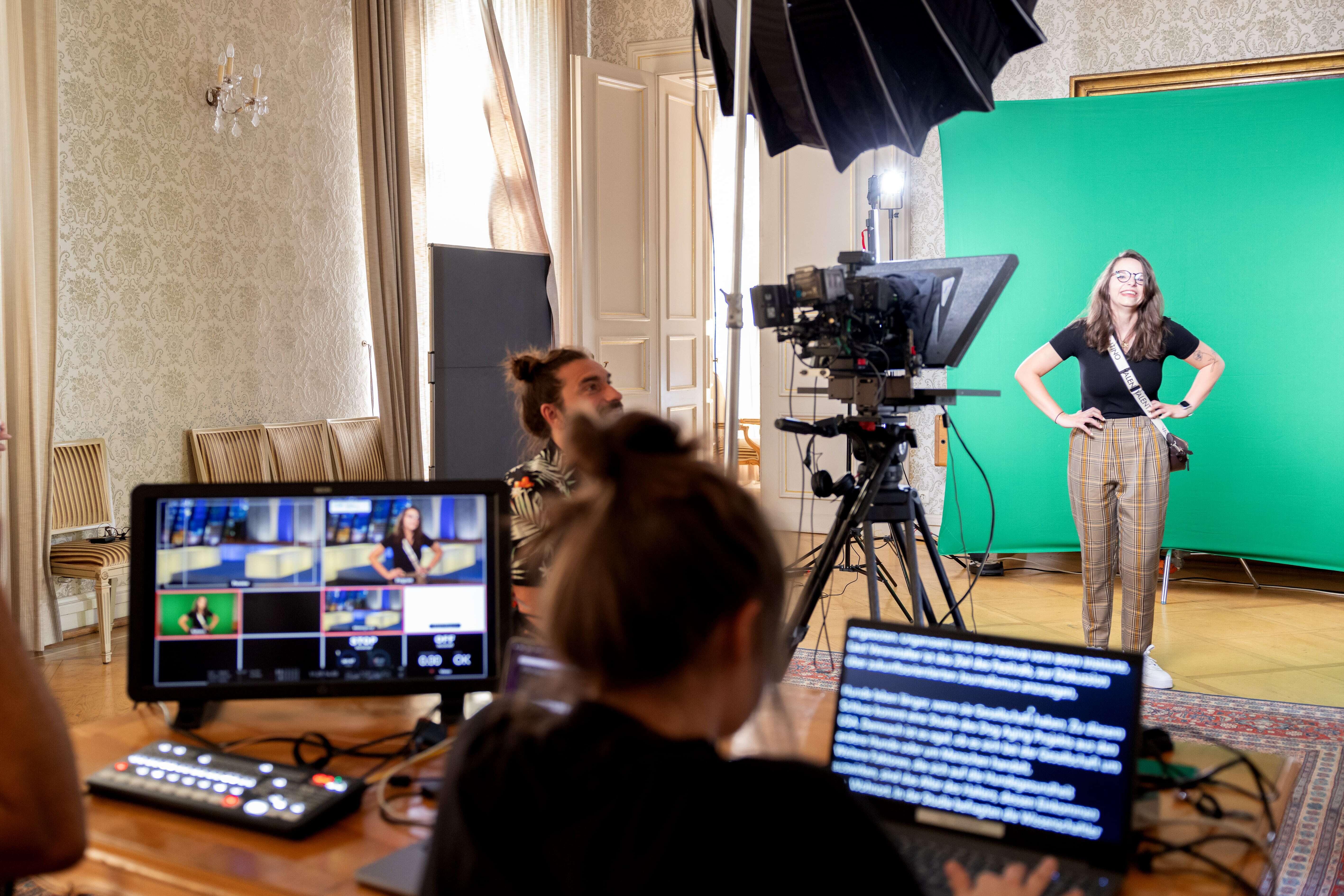 Vor einem Greenscreen und mit diversen Kameras und Bildschirmen führen einige Personen einen TV-Studio Workshop durch.