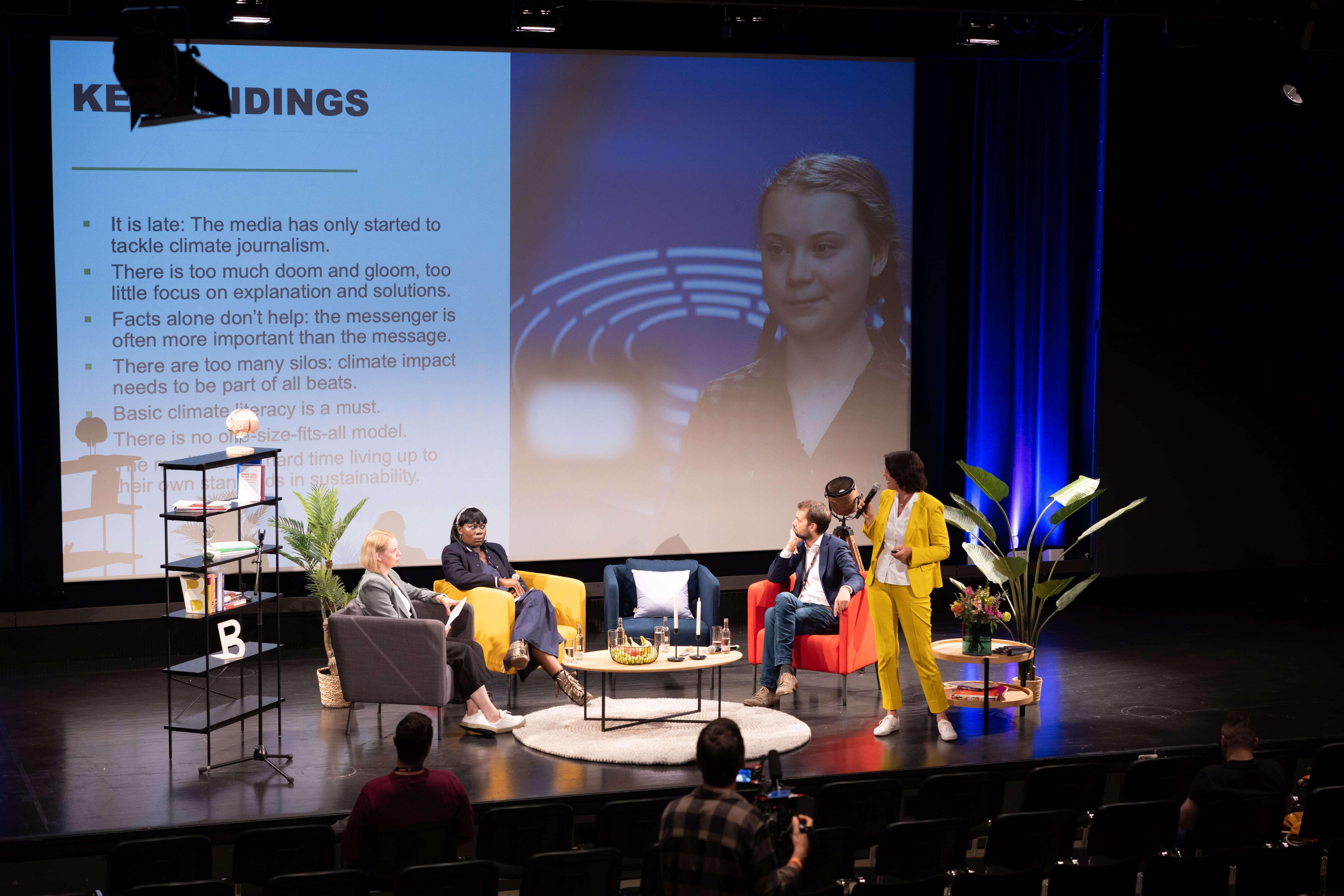 Alexandra Borchardt is giving a presentation; on the screen, there is an image of Greta Thunberg and the words "Key Findings." Lisa Urlbauer, Ruona Meyer, and Peter Schniering are sitting in chairs around her, listening