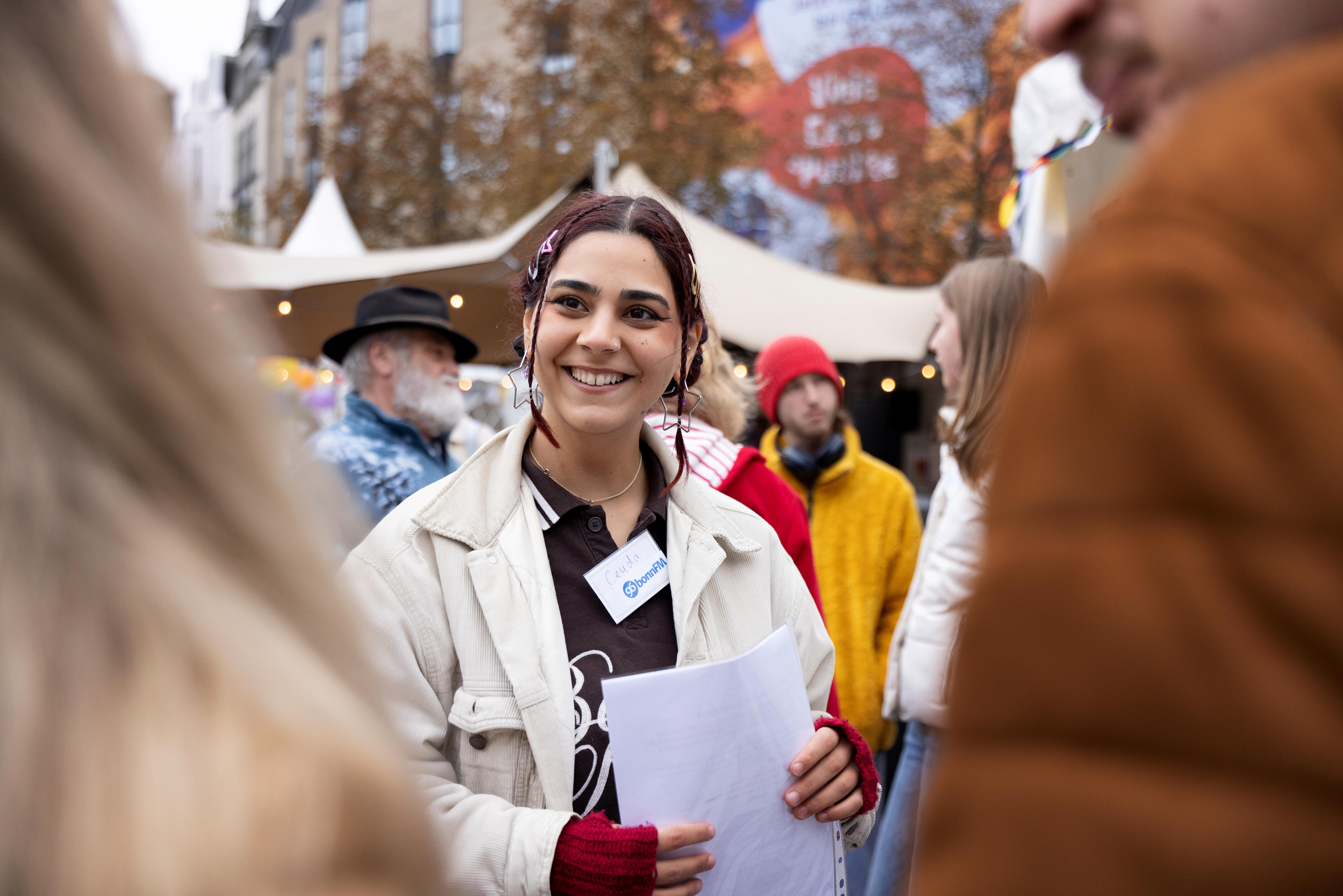 Eine lächelnde Frau steht auf dem Münsterplatz Menschen gegenüber. Sie hältPapierbögen in der Hand.