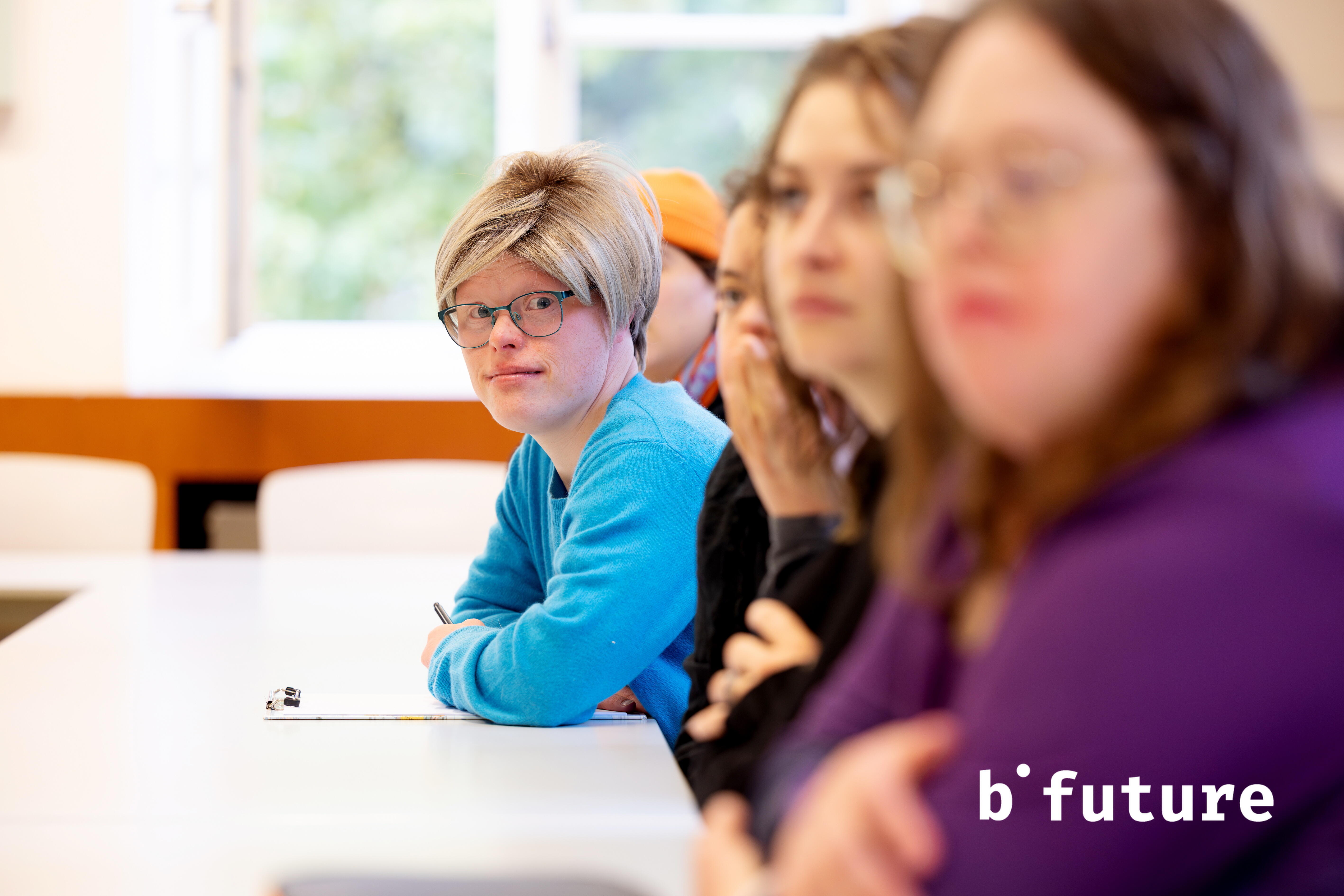 Eine Person sitzt mit anderen am Tisch und schaut seitlich in die Kamera