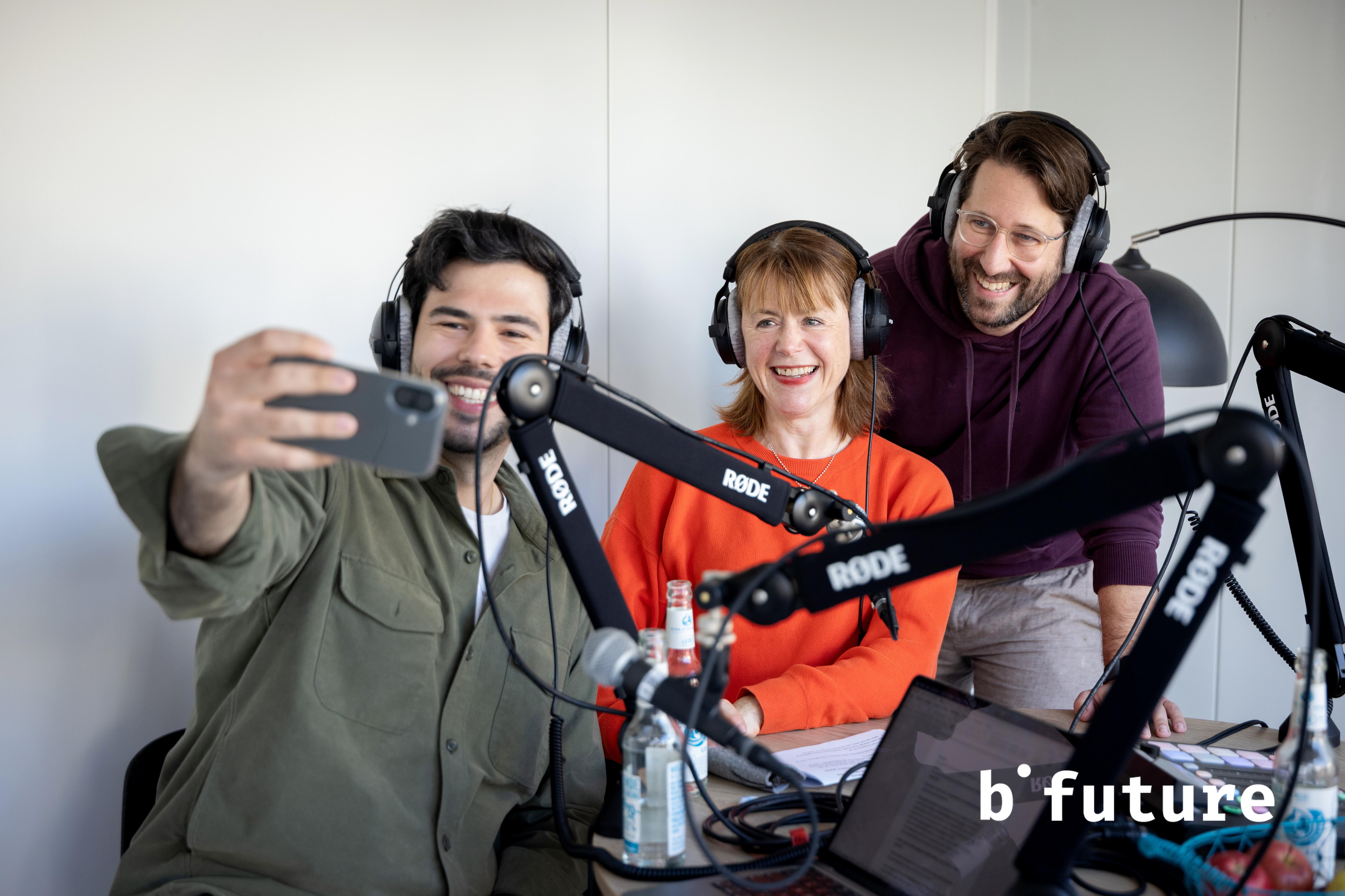 Drei Personen mit Kopfhörern nehmen ein Selfie auf und sitzen vor Mikrofonen