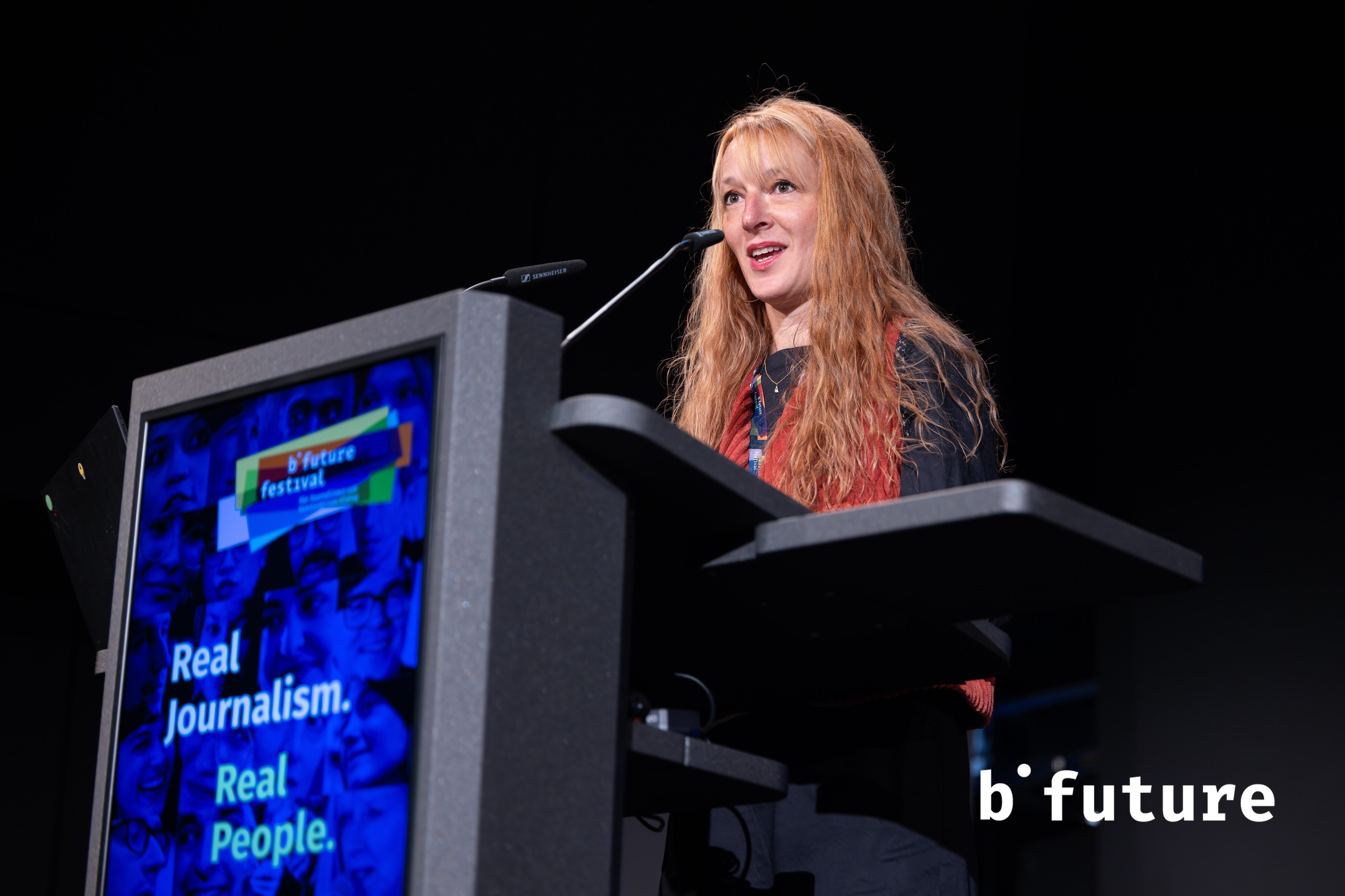 Nina Fasciaux steht hinter einem Rednerpult am Mikrofon und spricht hinein