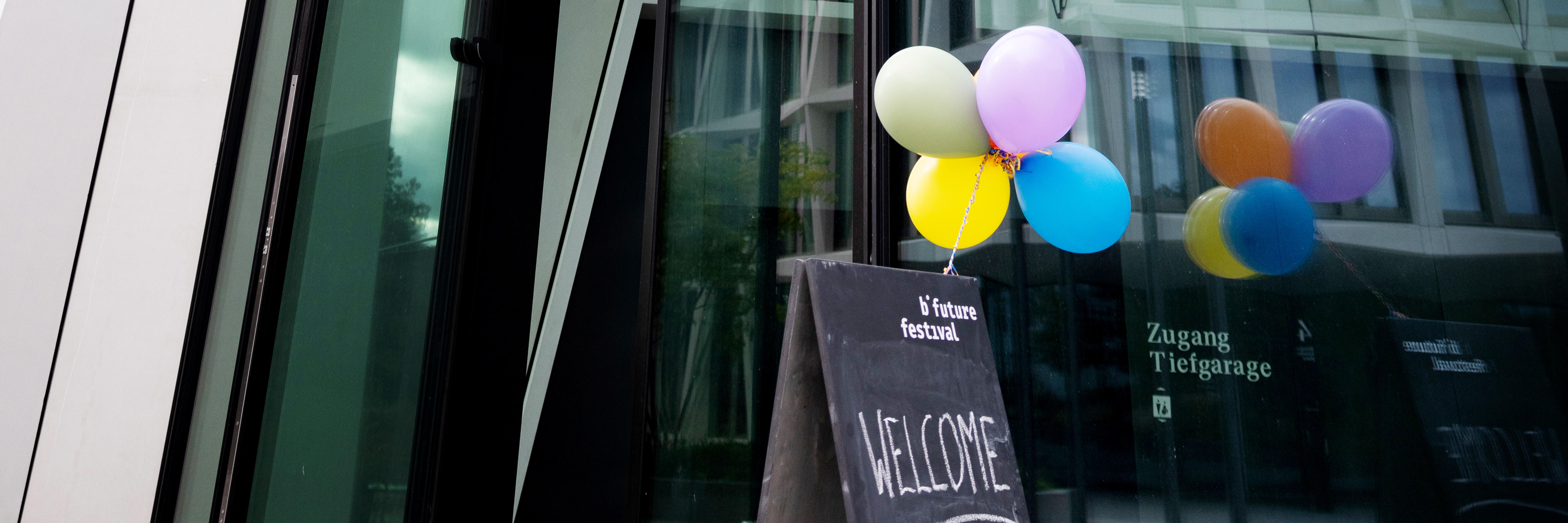 Ein Festivalaufsteller mit Ballons steht vor einer Glasfront eines Hauses.