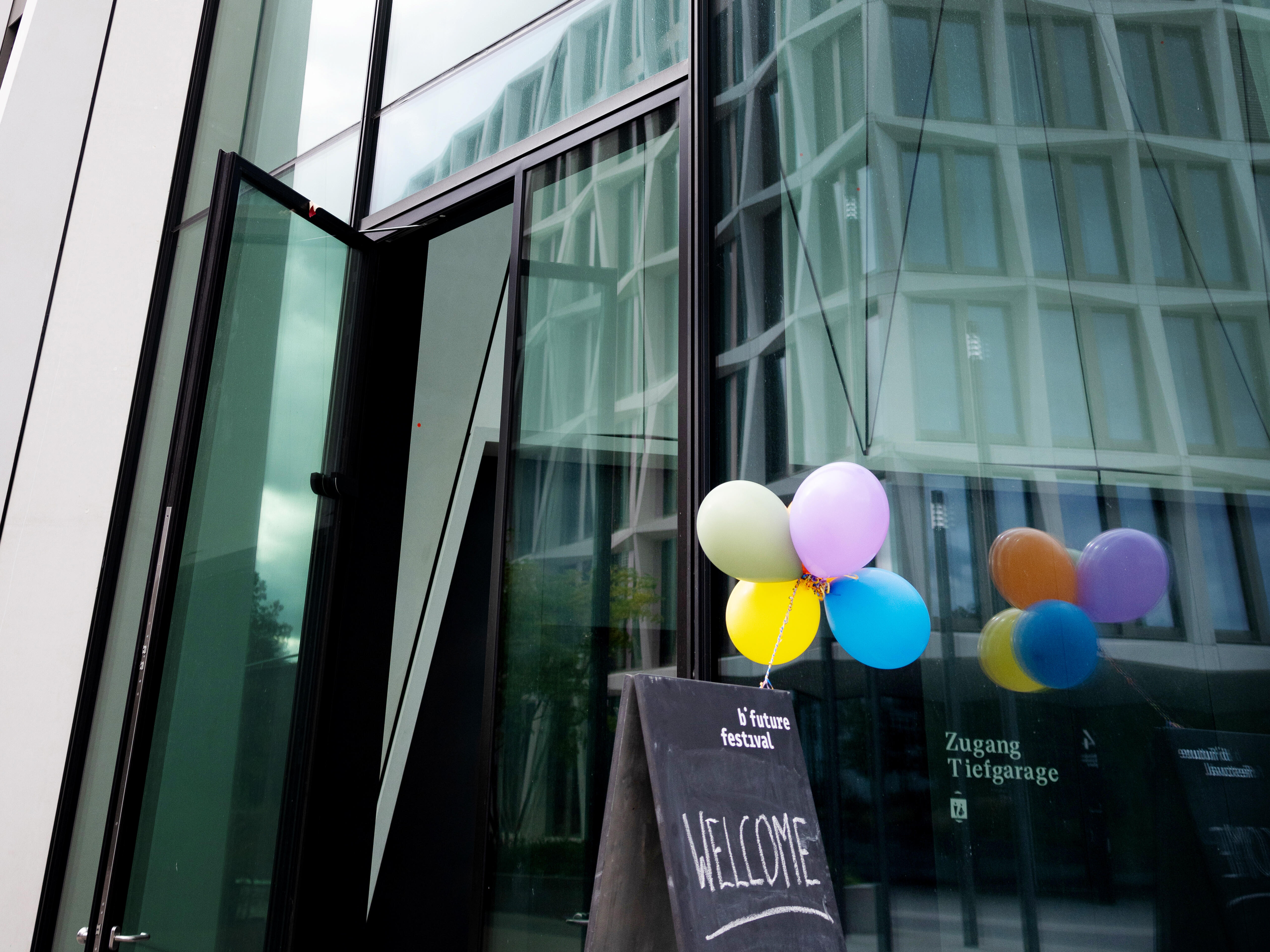 Ein Festivalaufsteller mit Ballons steht vor einer Glasfront eines Hauses.
