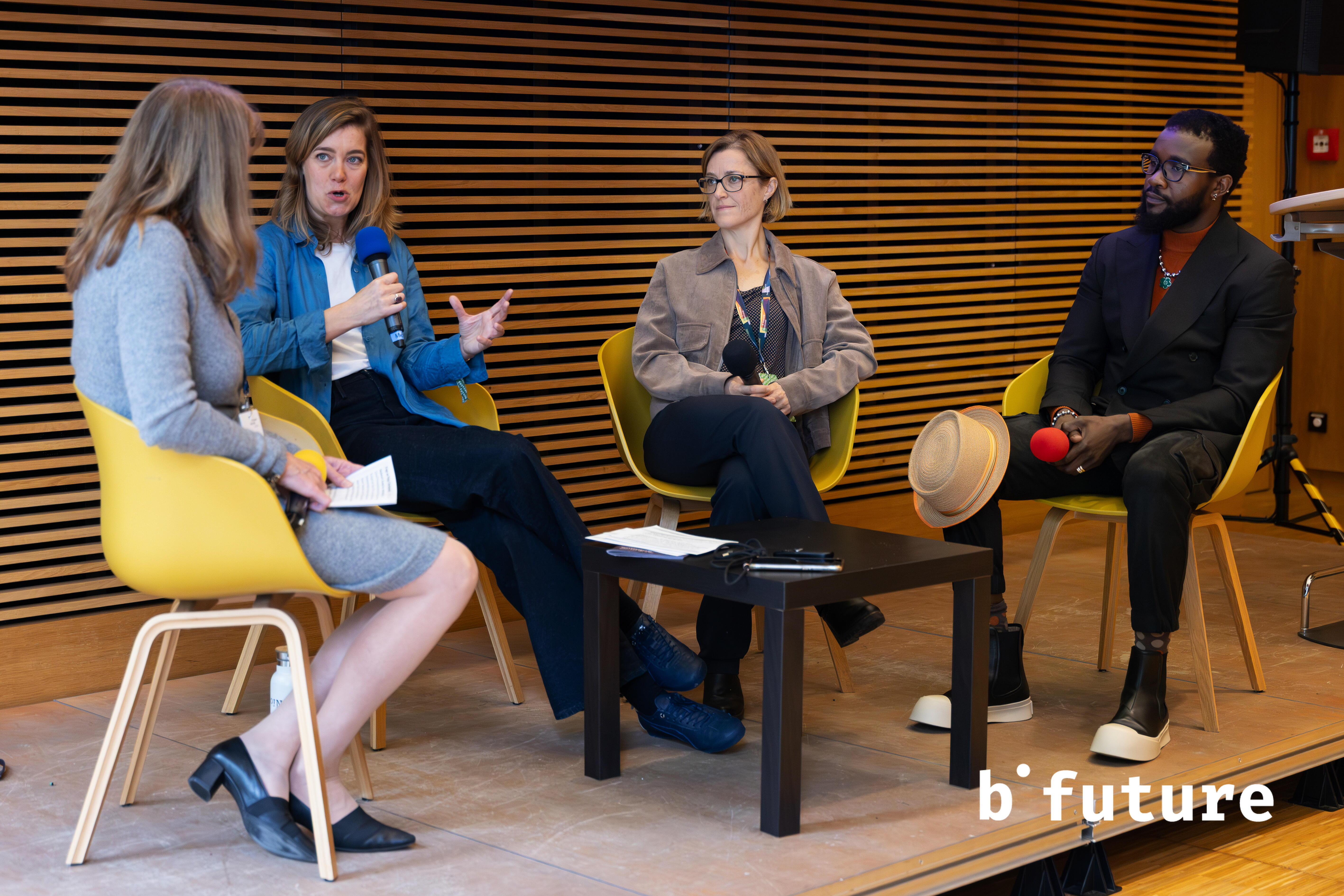 Vier Personen sitzen auf einer Bühne im Halbkreis zusammen. Eine Person spricht, die anderen schauen auf die sprechende Person.