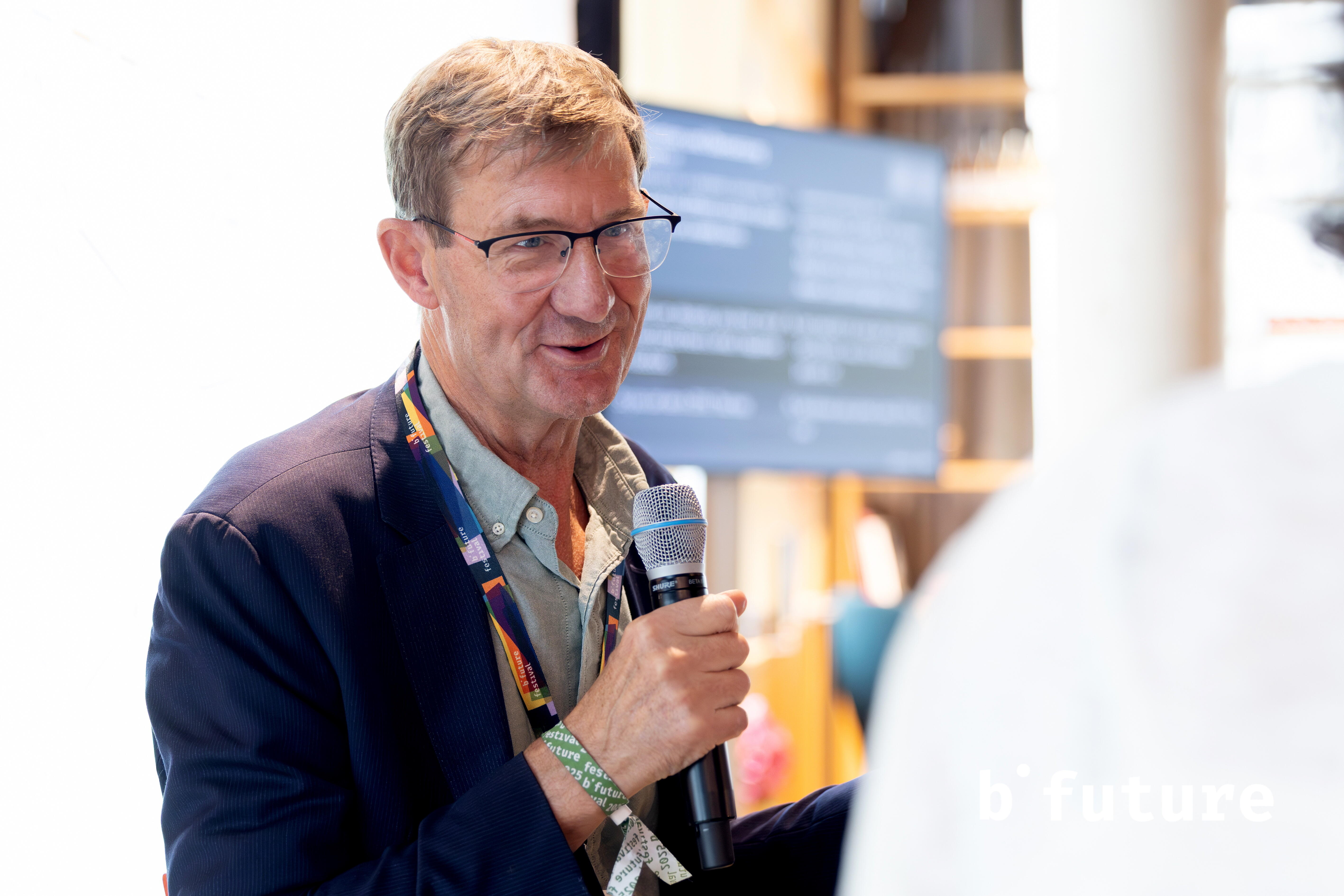 Nic Newman hält ein Mikrofon und spricht zu einer frontal-seitlich stehenden Person.