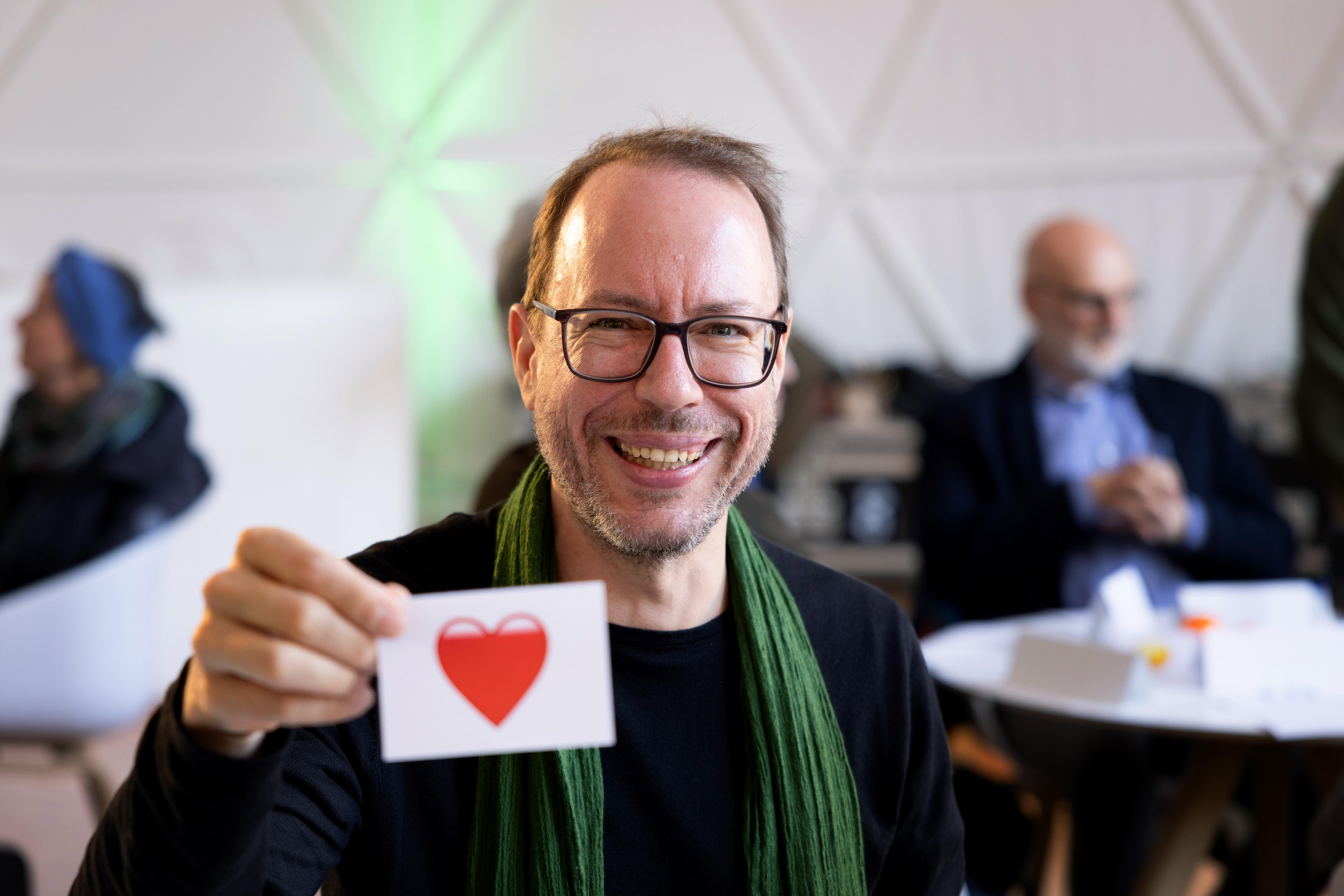 Markus Beckedahl holds a piece of paper with a heart in the Camera while smiling